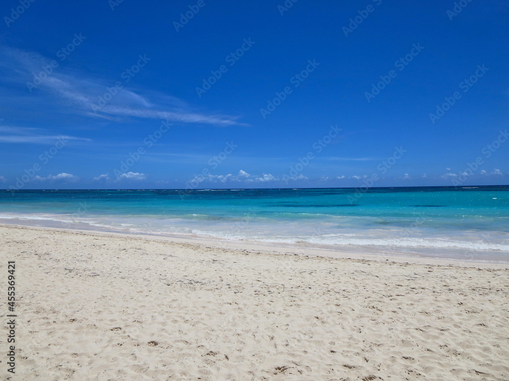 Photo of waves lapping empty Caribbean beach under bright blue sky.