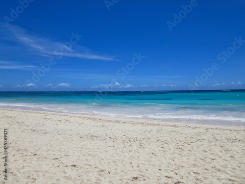 Photo of waves lapping empty Caribbean beach under bright blue sky.