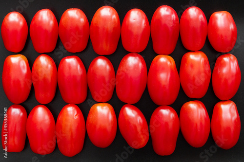 background: Red grape tomatoes or cherry tomatoes lie in three rows on black background.  Fresh tasty vegetables.