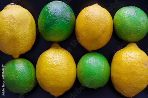 background: Lemon and lime fruits aligned alternately in two rows on black background top view
