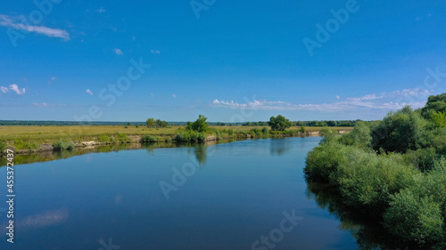 Aerial view of a beautiful summer landscape over river while dawn. Top view over river with a smooth water surface reflecting blue sky.