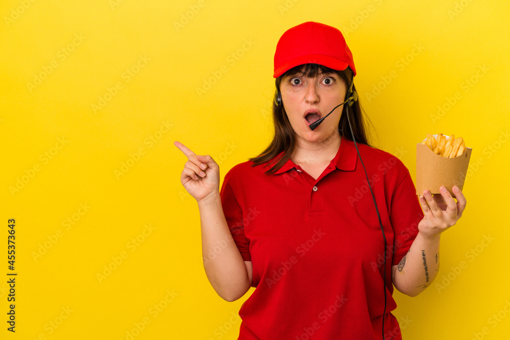 Young curvy caucasian woman fast food restaurant worker holding fries isolated on blue background pointing to the side