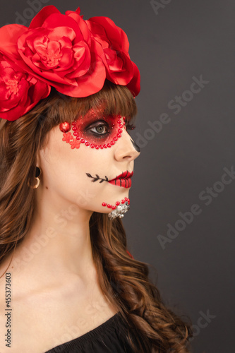 Profile portrait of a beautiful young girl with Dia de los Muertos makeup with gray background.