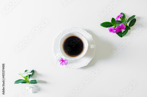 Black coffee cup, white flowers and blackberry tree leaves on white background. Flat lay, Top view. Spring concept.