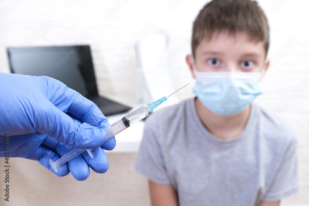 A boy getting vaccinated from covid-19, a doctor hold a syringe in order to vaccinate a teenager A boy getting vaccinated from covid-19, a doctor hold a syringe in order to vaccinate a teenager