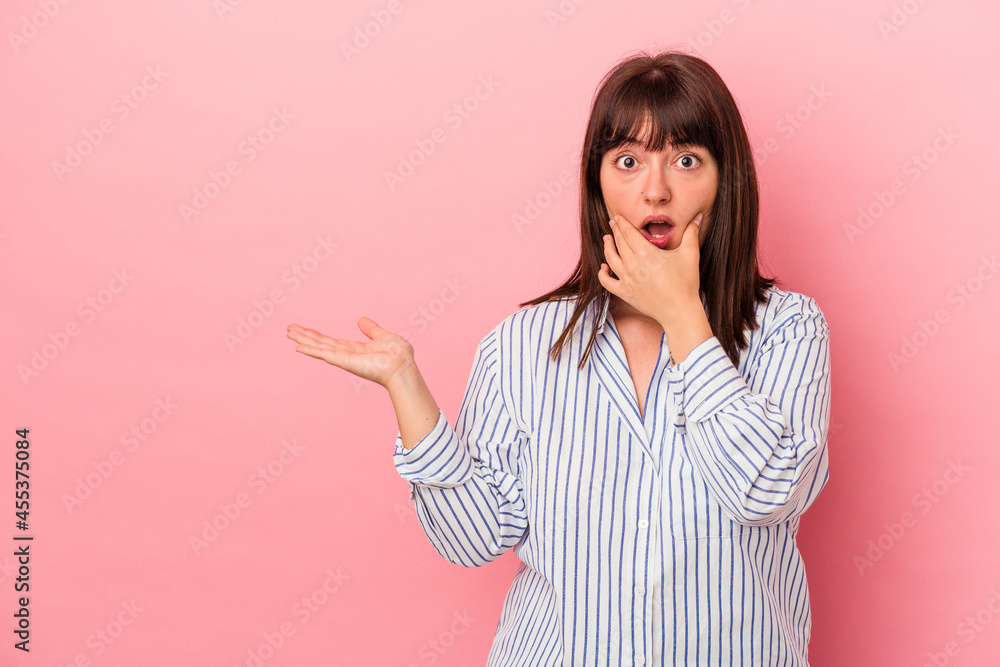 Young curvy caucasian woman isolated on pink background holds copy space on a palm, keep hand over cheek. Amazed and delighted. Young curvy caucasian woman isolated on pink background holds copy space on a palm, keep hand over cheek. Amazed and delighted.