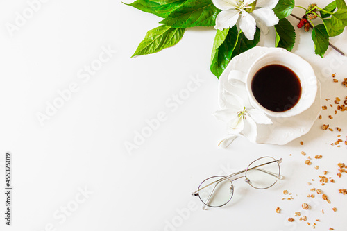 Black coffee cup, white flowers and blackberry tree leaves on white background. Flat lay, Top view. Spring concept.