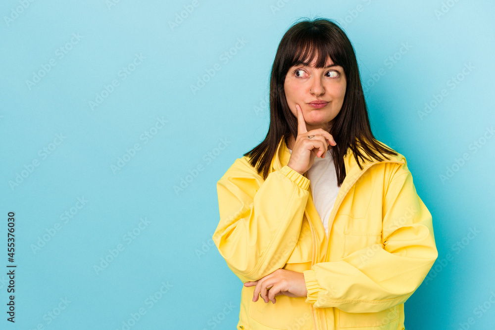 Young curvy caucasian woman isolated on blue background looking sideways with doubtful and skeptical expression.