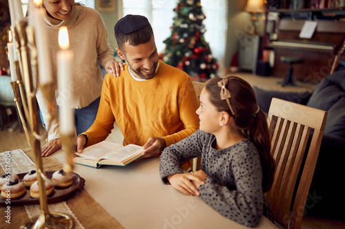 Happy Jewish family enjoys in reading Hebrew bible on Hanukkah at home.