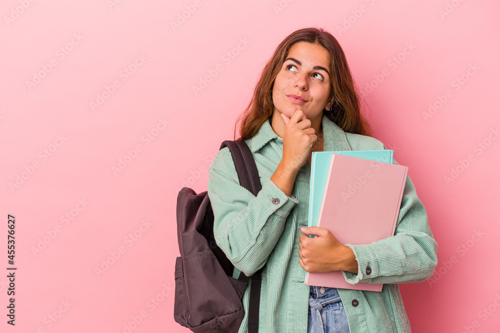 Young caucasian student woman holding books isolated on pink background looking sideways with doubtful and skeptical expression. Young caucasian student woman holding books isolated on pink background looking sideways with doubtful and skeptical expression.