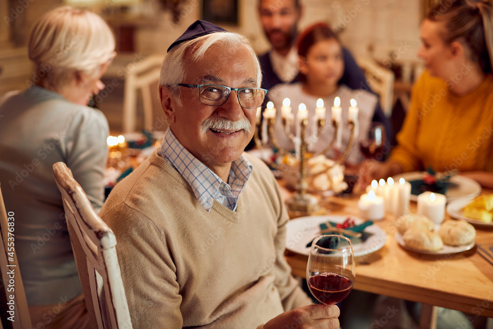 Happy Jewish senior man celebrates Hanukkah with his family at dining table.