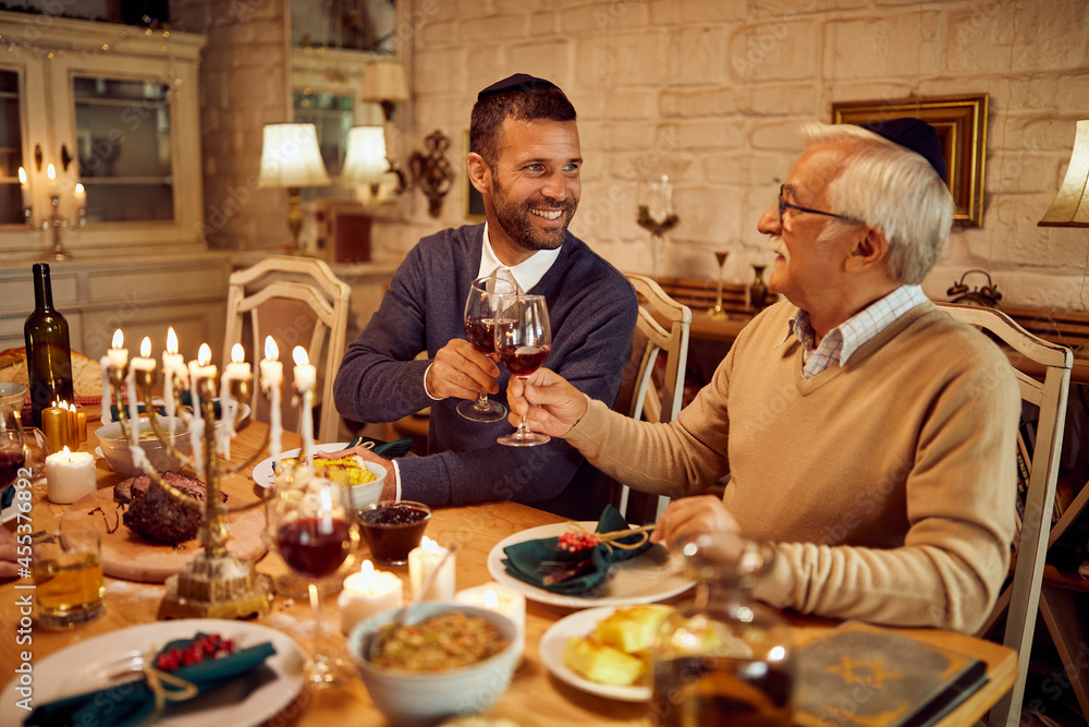 Happy Jewish men toast with wine at dining table while celebrating Hanukkah.