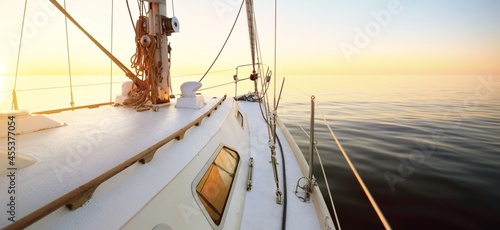 Yacht sailing in an open sea at sunset. Close-up view of the deck, mast and sails. Clear sky after the rain, glowing clouds, golden sunlight. Panoramic seascape photo