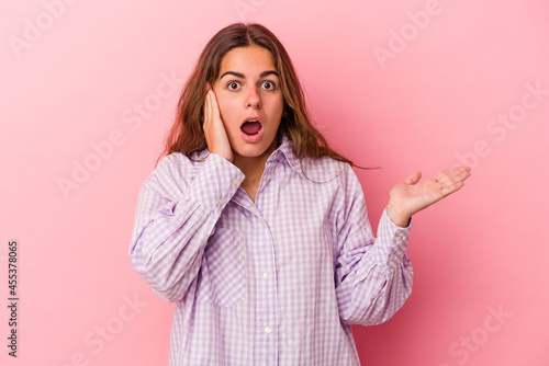 Young caucasian woman isolated on pink background impressed holding copy space on palm.
