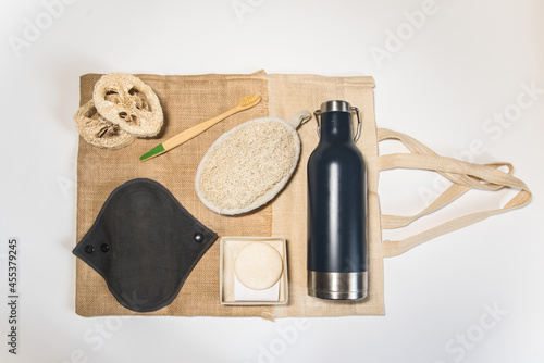 Artículos ecológicos sobre una bolsa tote bag. Botella de agua de acero inoxidable, esponja de lufa, compresa menstrual reutilizable, champú sólido, cepillo de dientes de bambú photo