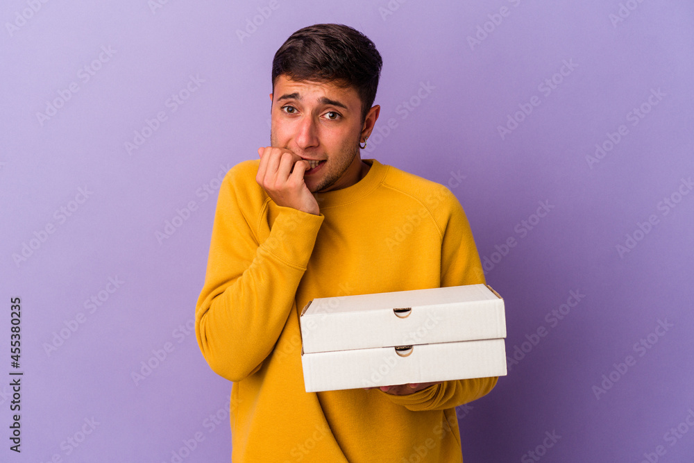 Young caucasian man holding pizzas isolated on purple background biting fingernails, nervous and very anxious. Young caucasian man holding pizzas isolated on purple background biting fingernails, nervous and very anxious.