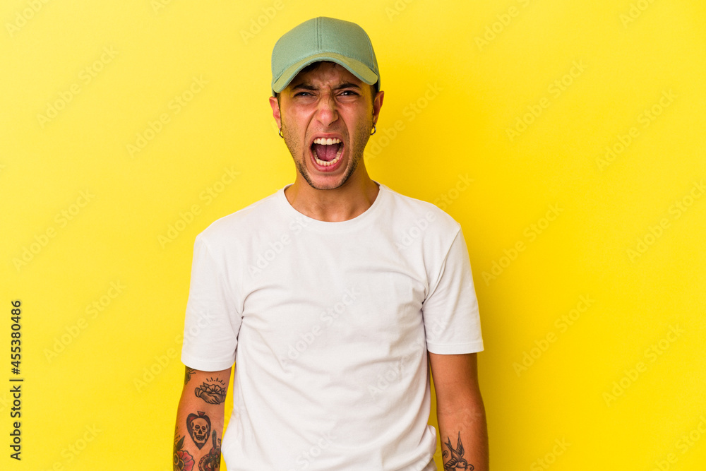 Young caucasian man with tattoos isolated on yellow background  shouting very angry, rage concept, frustrated.