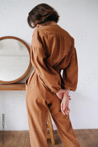 Back image of sexy woman in a brown jumpsuit holding hands behind her back