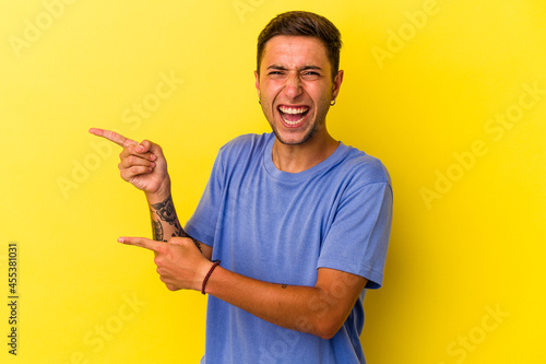 Young caucasian man with tattoos isolated on yellow background excited pointing with forefingers away.