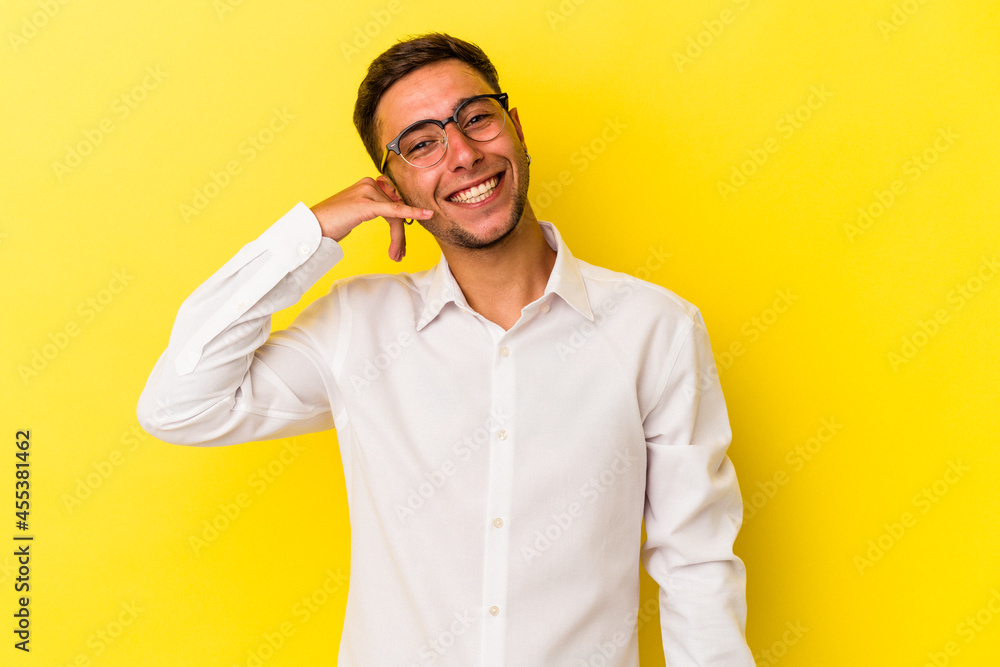 Young caucasian man with tattoos isolated on yellow background showing a mobile phone call gesture with fingers. Young caucasian man with tattoos isolated on yellow background showing a mobile phone call gesture with fingers.