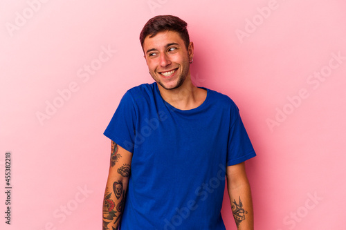 Young caucasian man with tattoos isolated on yellow background laughs and closes eyes, feels relaxed and happy.