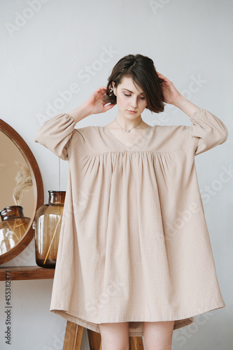 Thoughtful young woman in a beige dress fixing her hair, lifting her skirt up photo