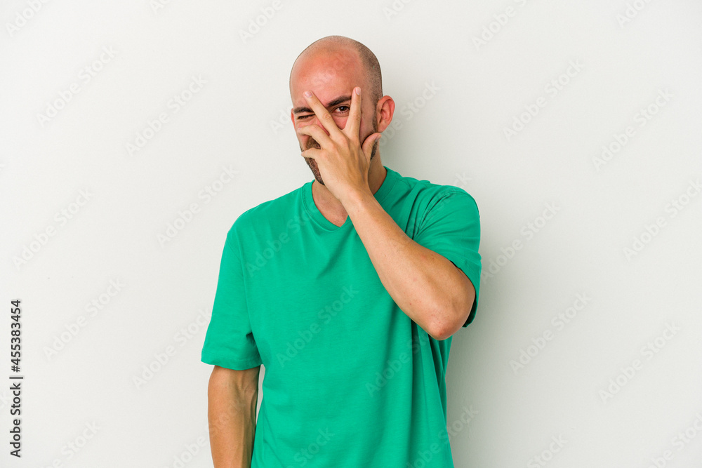 Young bald man isolated on white background blink at the camera through fingers, embarrassed covering face. Young bald man isolated on white background blink at the camera through fingers, embarrassed covering face.