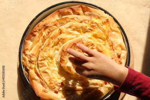 Child hand touching Bulgarian traditional baked dish with cheese, eggs and filo dough called banitza or banitsa photo