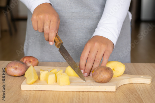 close up of a woman cutting a peeled potato in dices on a wood cutting board