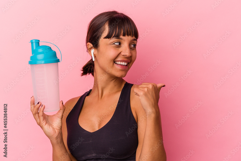 Young mixed race woman drinking protein shake isolated on pink background points with thumb finger away, laughing and carefree. Young mixed race woman drinking protein shake isolated on pink background points with thumb finger away, laughing and carefree.