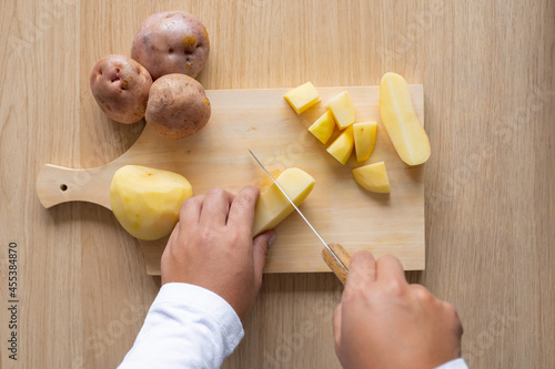 close up of a woman cutting a peeled potato in dices on a wood cutting board