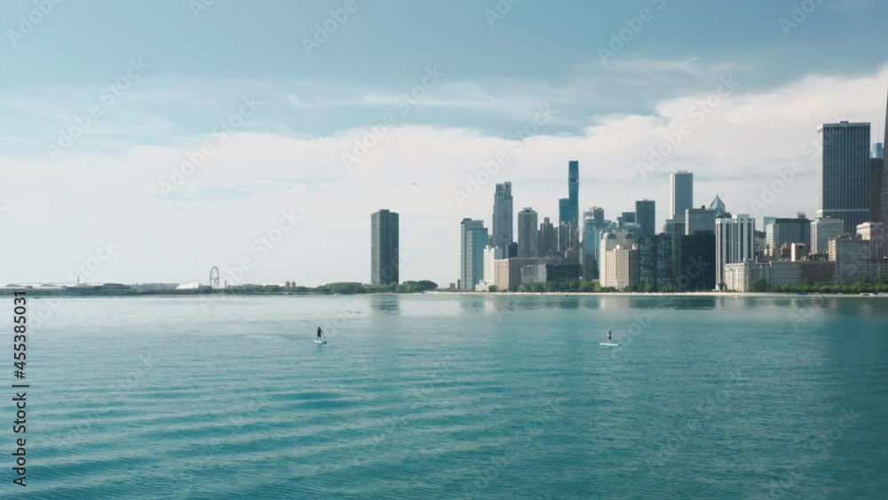 Man swimming on paddle board by Michigan lake with Chicago cityscape on motion background 4K. Cinematic aerial Chicago. Sunny summer day copy space on blue background. Modern water front buildings USA Man swimming on paddle board by Michigan lake with Chicago cityscape on motion background 4K. Cinematic aerial Chicago. Sunny summer day copy space on blue background. Modern water front buildings USA