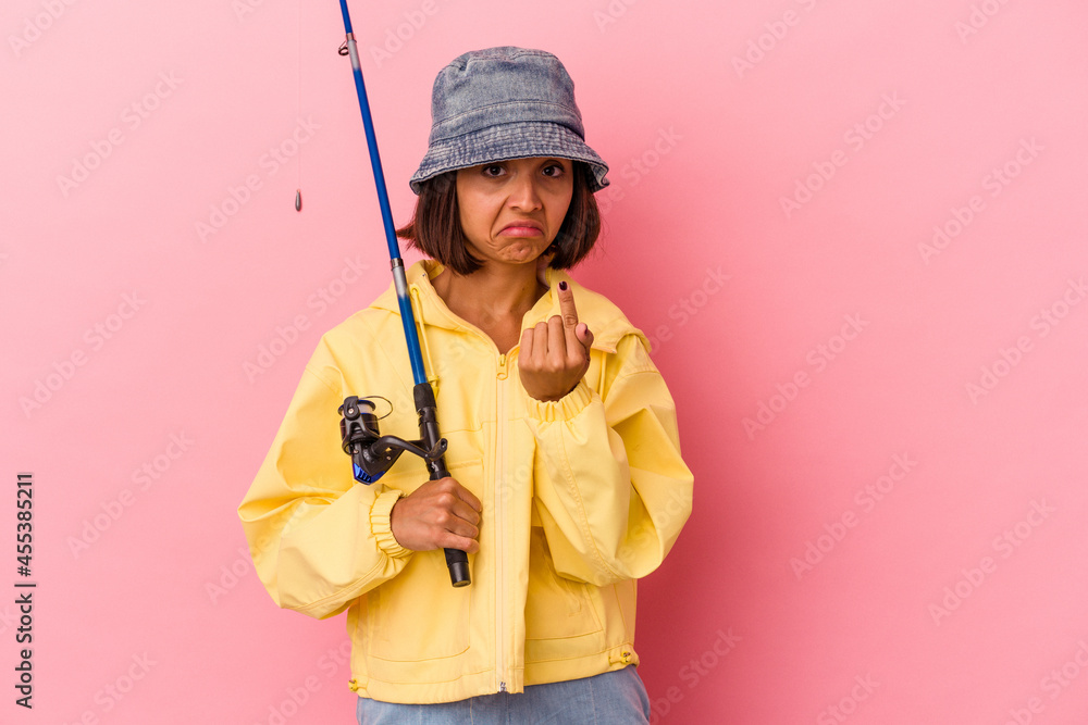 Young mixed race woman practicing fishing isolated on pink background pointing with finger at you as if inviting come closer. Young mixed race woman practicing fishing isolated on pink background pointing with finger at you as if inviting come closer.