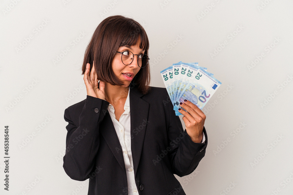 Young mixed race business woman holding a banknotes isolated on white background trying to listening a gossip. Young mixed race business woman holding a banknotes isolated on white background trying to listening a gossip.