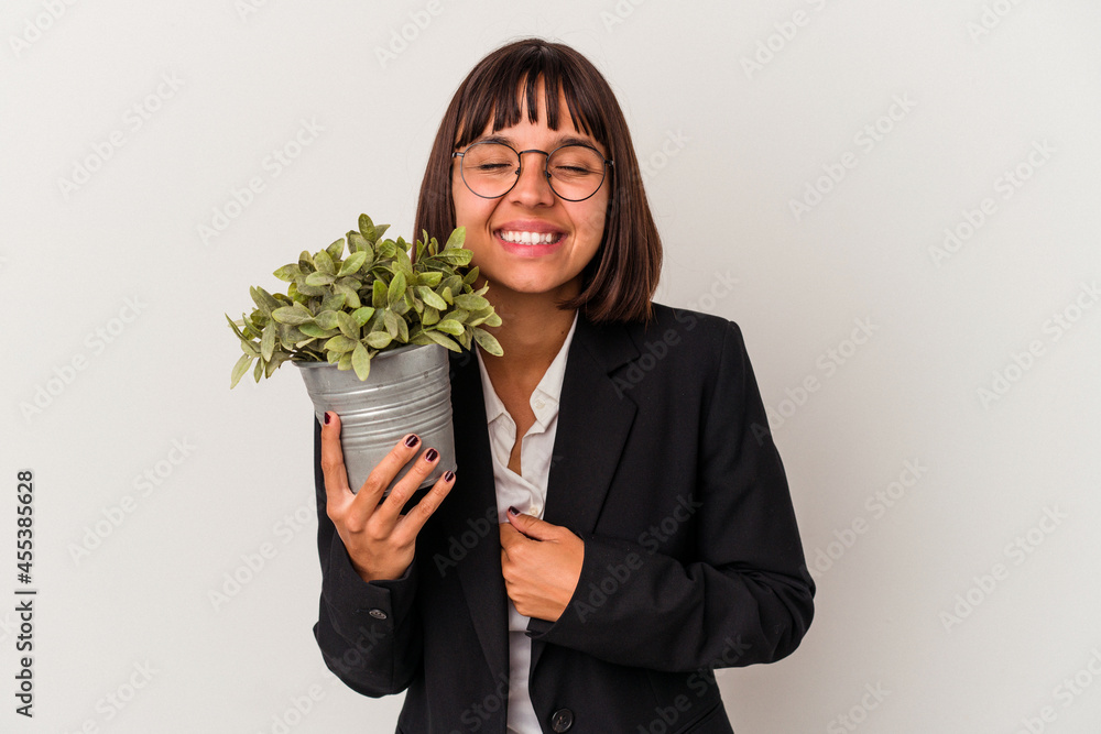 Young mixed race business woman holding a plant isolated on white background laughing and having fun. Young mixed race business woman holding a plant isolated on white background laughing and having fun.