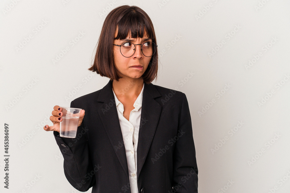 Young mixed race business woman holding a glass of water isolated on white background confused, feels doubtful and unsure. Young mixed race business woman holding a glass of water isolated on white background confused, feels doubtful and unsure.