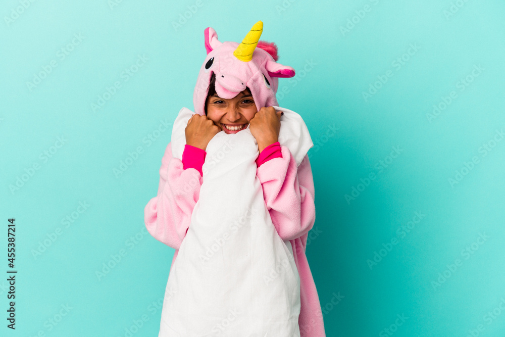 Young mixed race woman wearing a unicorn pajama holding a pillow isolated on blue background