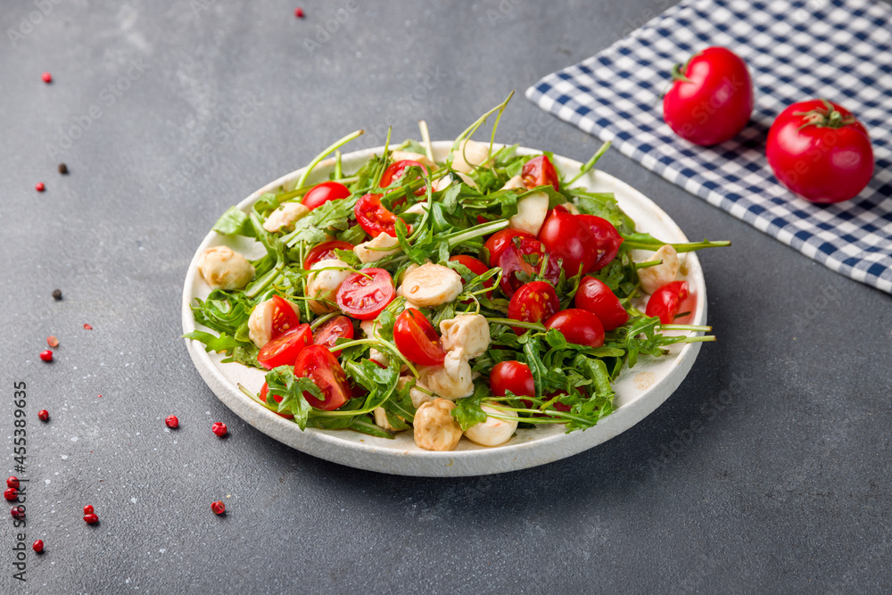 Salad with mozzarella, tomatoes and arugula on white plate Salad with mozzarella, tomatoes and arugula on white plate