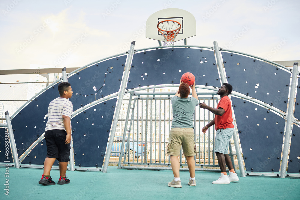 Boy throwing ball into basketball hoop under fathers control while