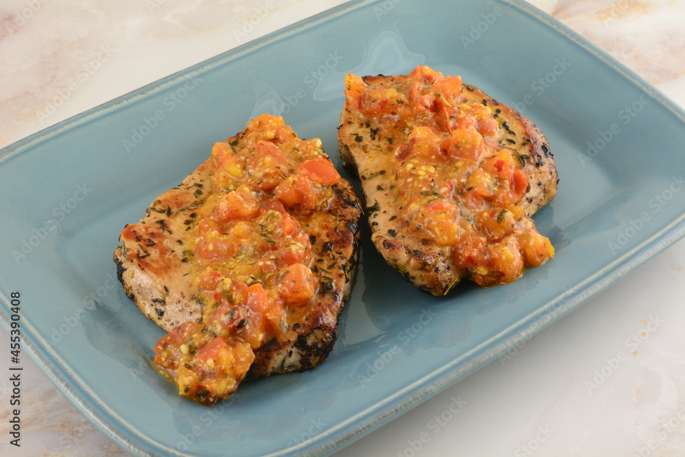 Two boneless pork chops with spicy tomato and red pepper sauce on blue serving plate Two boneless pork chops with spicy tomato and red pepper sauce on blue serving plate