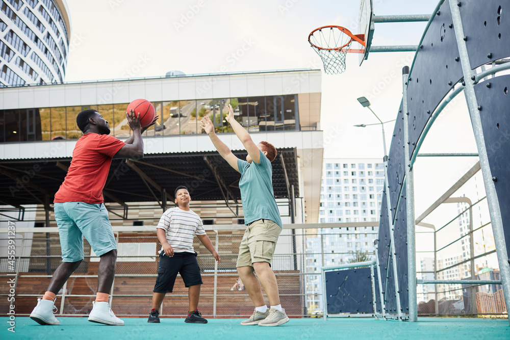 Boy Raising hands while making cuts under hoop while playing basketball with brothers on city playground