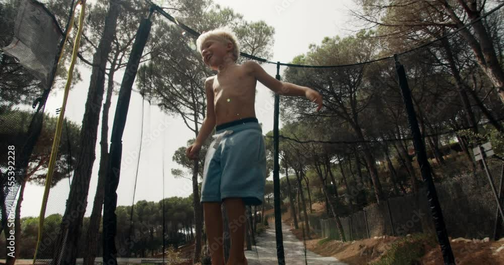 Little 4 years blonde boy is having fun during his summer vacations jumping on trampoline in forest of rural house terrain and smiling. Catalonia, Spain Little 4 years blonde boy is having fun during his summer vacations jumping on trampoline in forest of rural house terrain and smiling. Catalonia, Spain