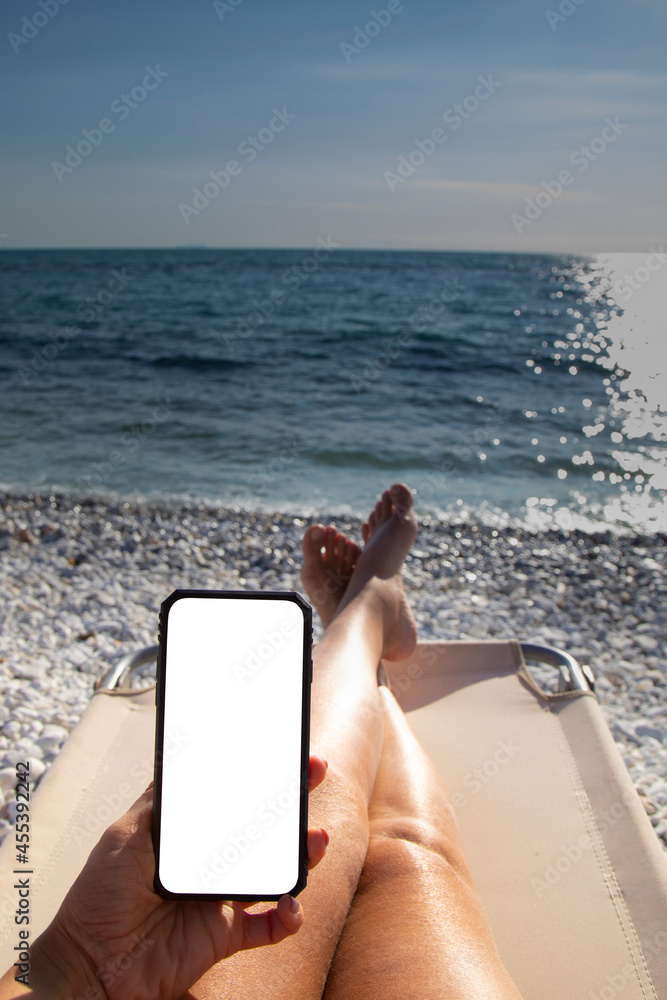 the hand with the mobile phone of a woman on vacation on the sun bed on the beach by the sea