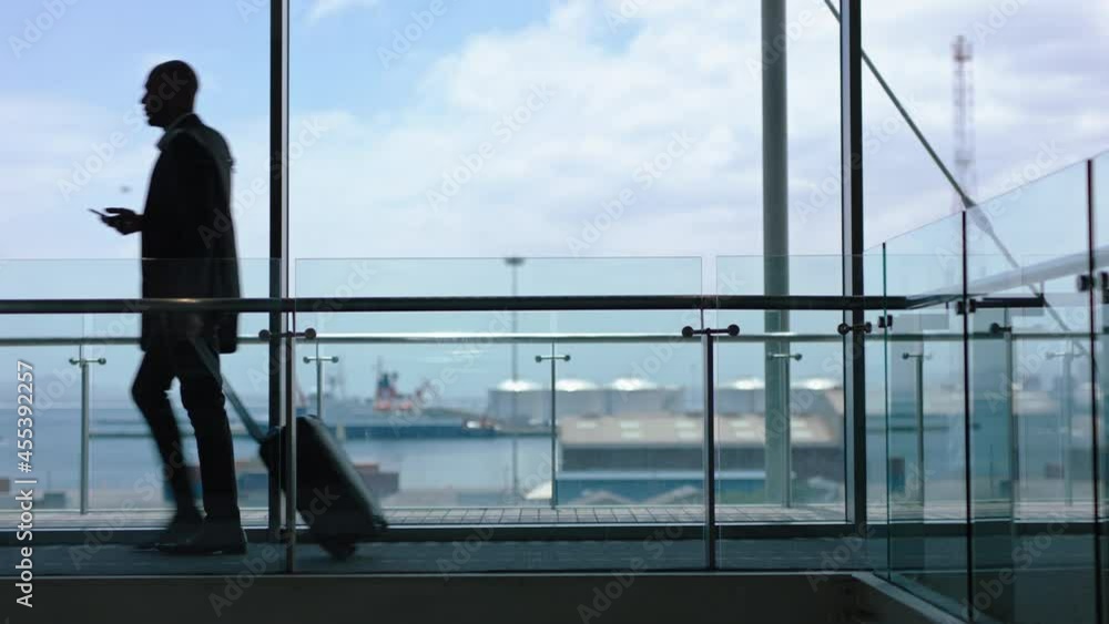 businessman walking with trolley bag using smartphone traveling for international business trip in airport lobby with view of harbor port 4k footage businessman walking with trolley bag using smartphone traveling for international business trip in airport lobby with view of harbor port 4k footage