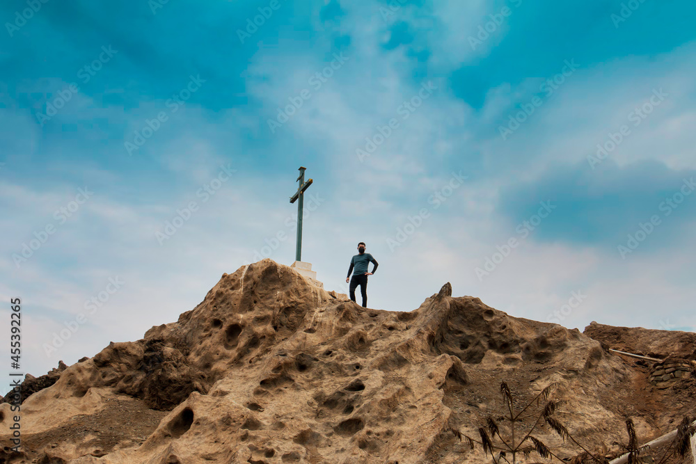 Man stands in front of a cross on a mountain.