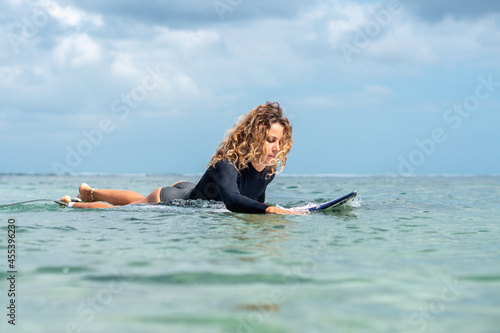 Portrait of surfer girl on white surf board in blue ocean pictured from the water