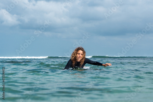 Portrait of surfer girl on white surf board in blue ocean pictured from the water © Lila Koan