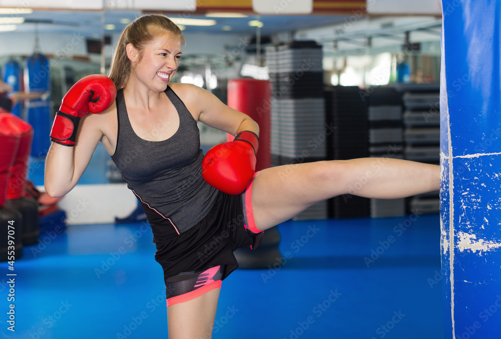 Portrait of young woman who is training with punching bag in box gym