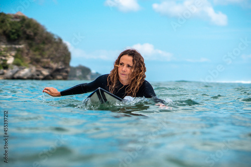 Portrait of surfer girl on white surf board in blue ocean pictured from the water