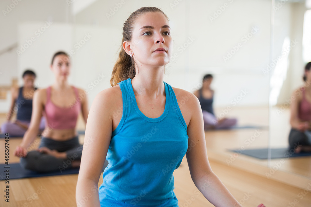 Portrait of young european female making yoga meditation in lotus pose in fitness studio